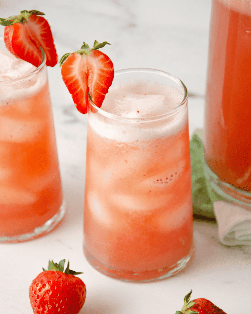 A pink strawberry agua fresca in a tall glass with a strawberry garnish.