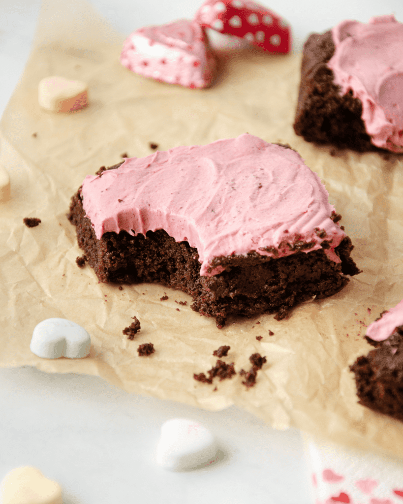 A gluten free brownie with a pink creamy topping with a bite taken out.