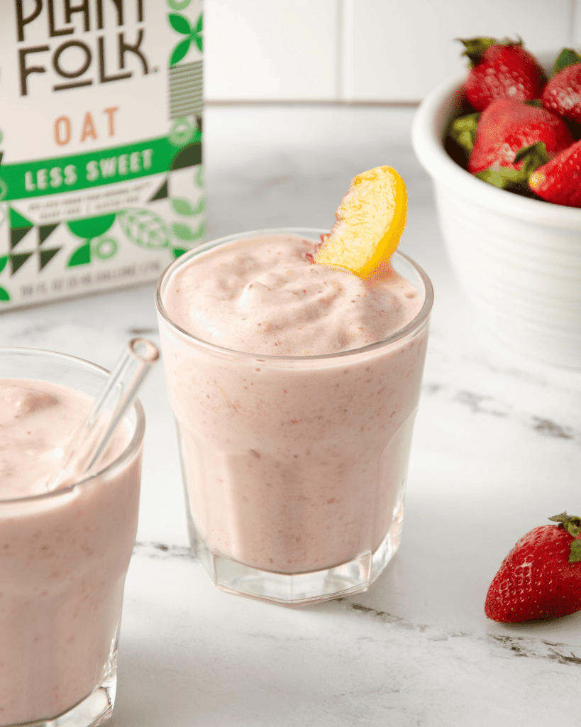 A pink smoothie with a bright yellow peach in a glass with a marble background.